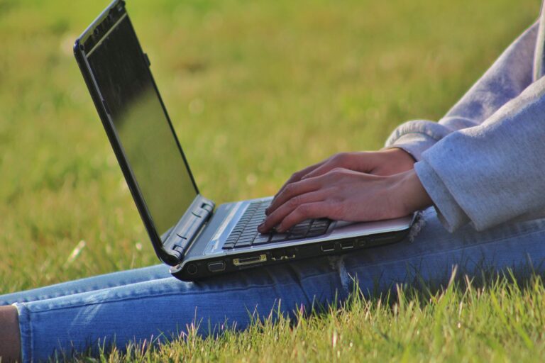 Image of a person working on a laptop whilst sitting outside on a playing field