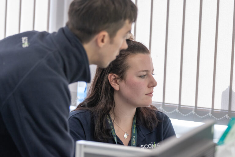 Close up of two Scomis staff members looking at a screen